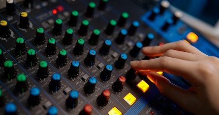 Side view closeup audio engineer hand on sound mixer control panel inside production house